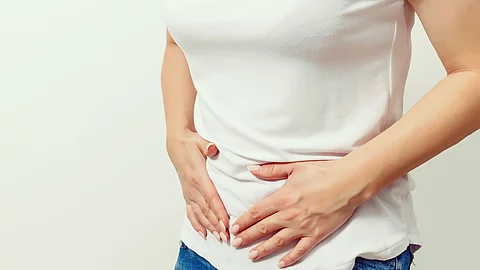 Frau in Jeans und weißem T-Shirt hält sich den Bauch