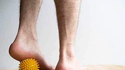 Füße, die über einen gelben Massageball mit Noppen rollen.