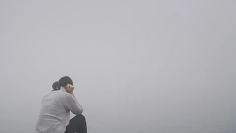 Junge Frau sitzt einsam am Rand eines Holzweges einer Brücke g Junge Frau sitzt gekrümmt an einem Steg und vergräbt ihr Gesicht hinter ihren Händen.