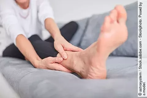 Frau sitzt auf Sofa und reibt sich den Fuß.
