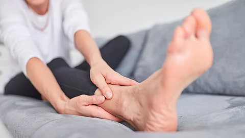 Frau sitzt auf Sofa und reibt sich den Fuß.