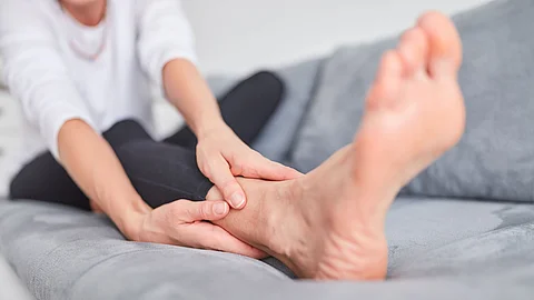Frau sitzt auf Sofa und reibt sich den Fuß.