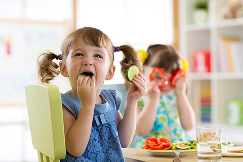 2 Mädchen am Esstisch essen Gemüse