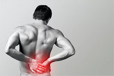 Schwarz-weiß-Bild eines Mannes mit freiem Oberkörper, der sich den schmerzenden unteren Rücken hält