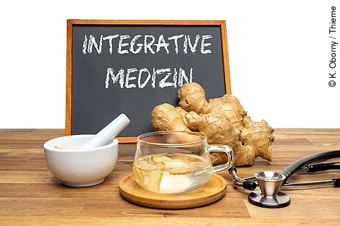 Symbolbild Integrativmedizin: Ingwer, Stethoskop, Ingwertee auf Holztisch, dahinter eine Tafel mit der Aufschrift "Integrative Medizin"