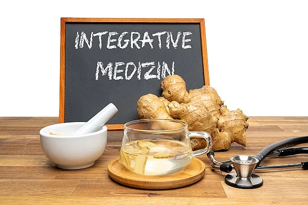 Symbolbild Integrativmedizin: Ingwer, Stethoskop, Ingwertee auf Holztisch, dahinter eine Tafel mit der Aufschrift "Integrative Medizin"