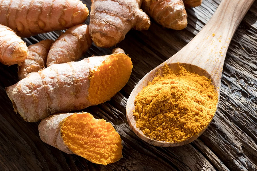Ground turmeric on a wooden spoon, with fresh turmeric root in the background Kurkumawurzel und -pulver auf Holzlöffel