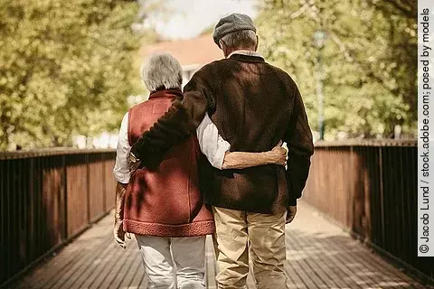 Seniorenpaar spaziert Arm in Arm durch einen Park 