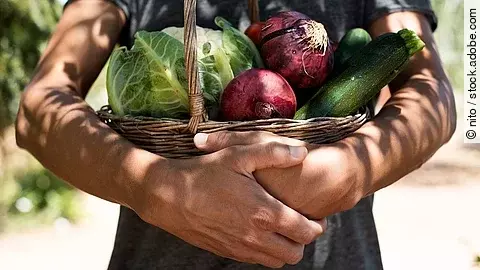 Ein Mann hält einen Korb mit frisch geerntetem Gemüse