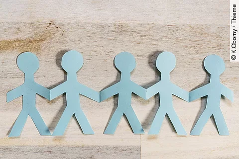 Girlande aus Papiermännchen liegt auf einem hölzernen Untergrund. 