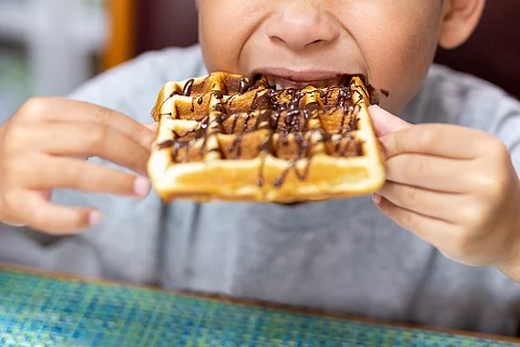 Kind beißt in Waffel mit Schokosoße