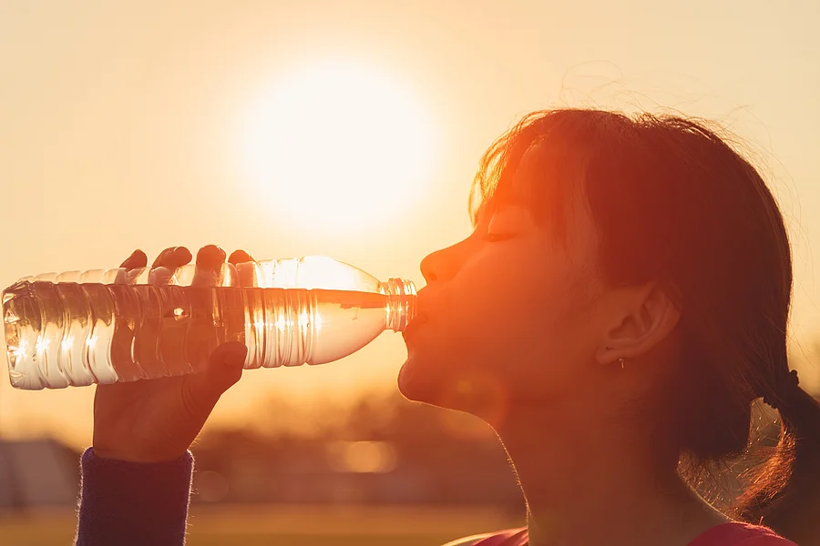 Eine Frau trinkt in der Sonnenhitze aus einer Flasche Wasser Eine Frau trinkt in der Sonnenhitze aus einer Flasche Wasser