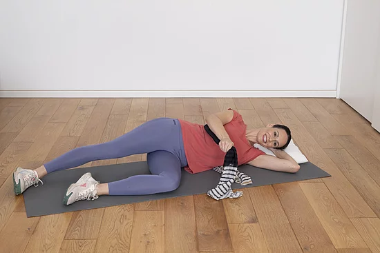 Junge Frau liegt seitlich auf Yogamatte und macht Atemübungen.