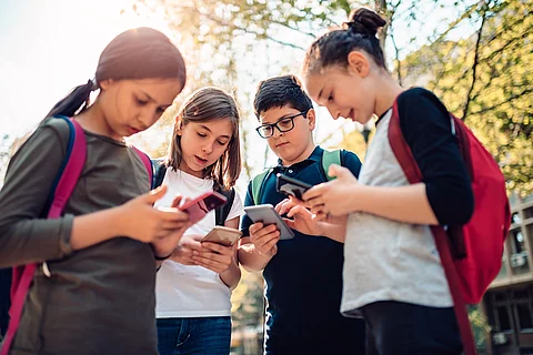 Eine Gruppe von Kindern hängt nach der Schule auf der Straße ab und benutzt an einem sonnigen Tag ihre Smartphones.