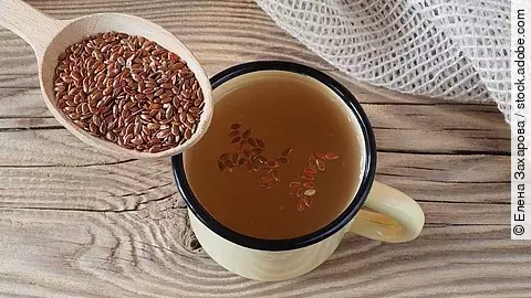 Ein Löffel mit Leinsamen, daneben eine Tasse mit eingeweichten Leinsamen auf Holzuntergrund