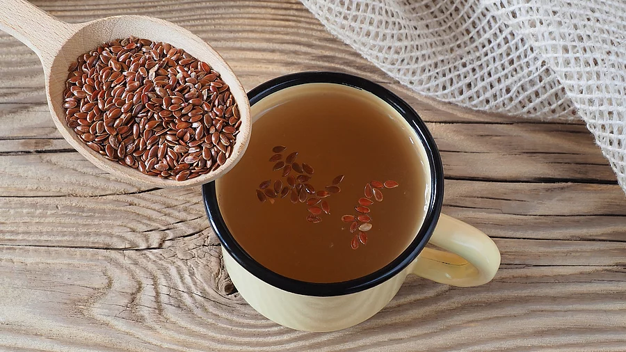 Ein Löffel mit Leinsamen, daneben eine Tasse mit eingeweichten Leinsamen auf Holzuntergrund