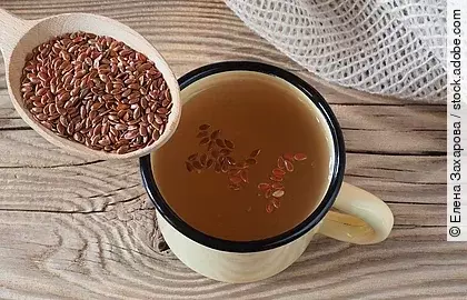 Ein Löffel mit Leinsamen, daneben eine Tasse mit eingeweichten Leinsamen auf Holzuntergrund