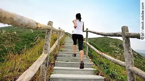 Frau rennt in Sportkleidung die Stufen an einem Berg hoch.