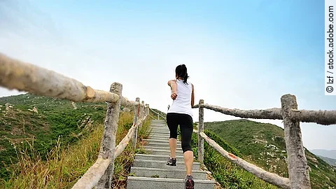 fitness woman running up at stone stairs to mountain peak Frau rennt in Sportkleidung die Stufen an einem Berg hoch.