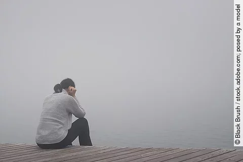 Junge Frau sitzt am Rand eines Holzwegs. traurig