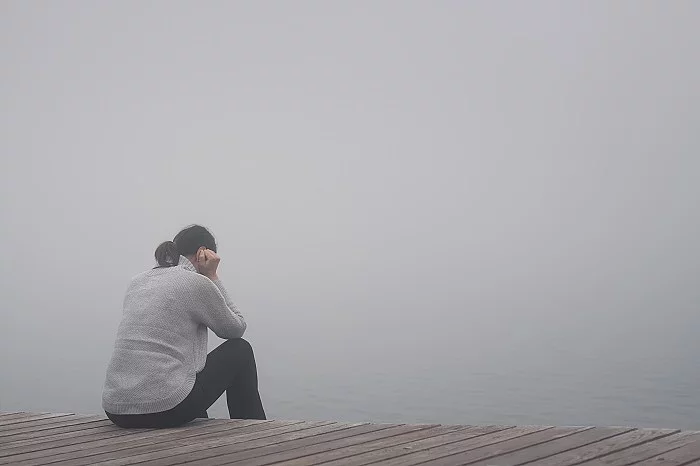 Junge Frau sitzt einsam am Rand eines Holzweges einer Brücke g Junge Frau sitzt am Rand eines Holzwegs. traurig