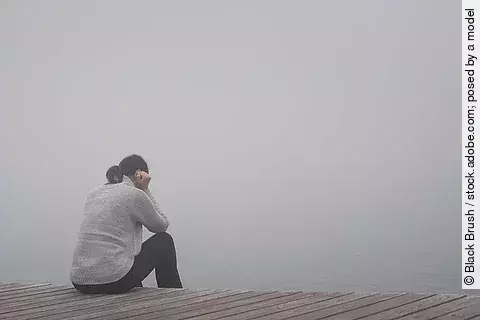 Junge Frau sitzt am Rand eines Holzwegs. traurig