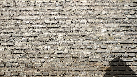 Schatten eines sitzenden Menschen mit Kopf auf den Knien vor einer Mauer