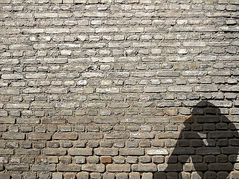 Schatten eines sitzenden Menschen mit Kopf auf den Knien vor einer Mauer