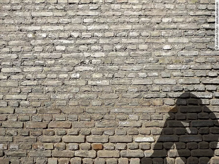 Schatten eines sitzenden Menschen mit Kopf auf den Knien vor einer Mauer