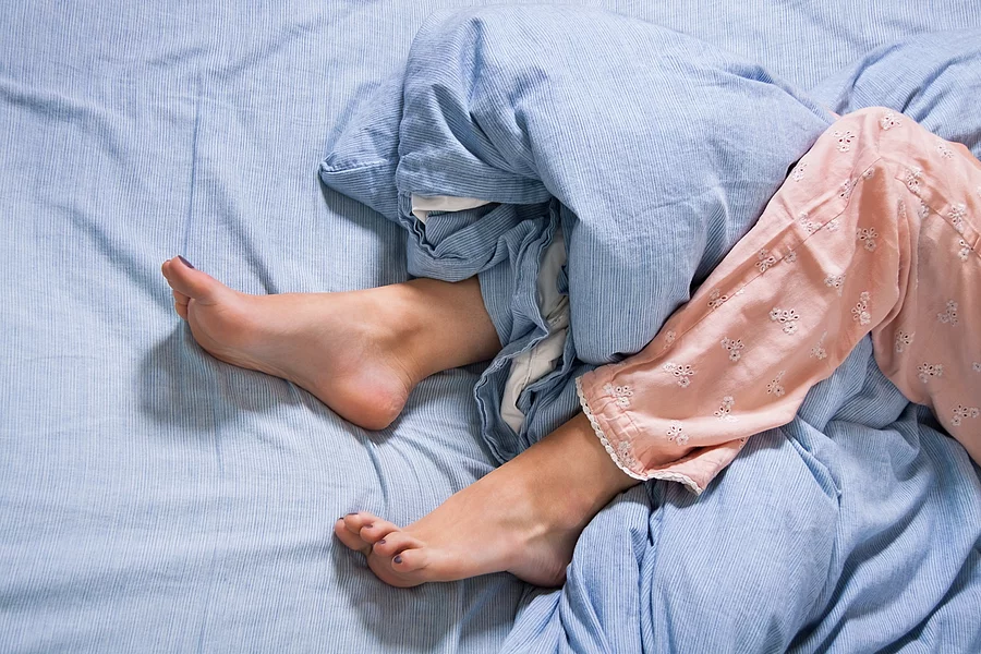 Weibliche Füße mit Schlafanzug in einem Bett