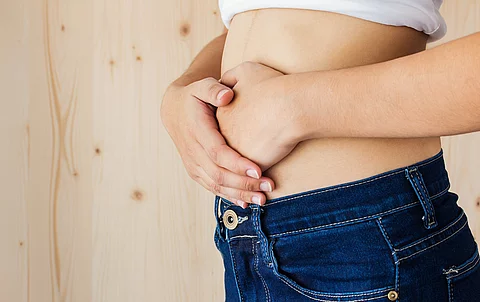 Frau in Jeans hat beide Hände auf dem Bauch