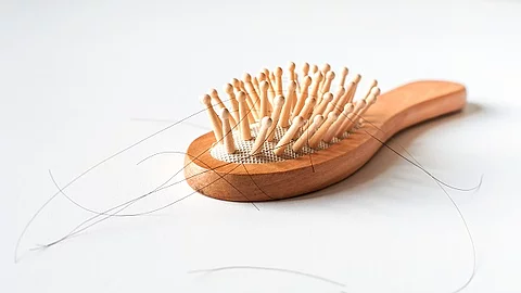 Haarbürste aus Holz mit ausgefallenen Haaren auf weißem Hintergrund