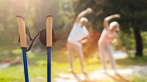 Ein älteres Ehepaar macht Sportübungen im Hintergrund (verschwommen). Im Vordergrund sind Walking Stöcke zu sehen.