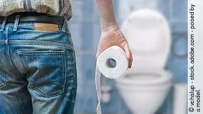 Mann von hinten mit Klorolle, steht vor einer Toilette