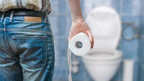 Mann von hinten mit Klorolle, steht vor einer Toilette