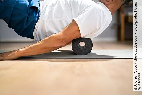 Ein Mann rollt seinen Rücken über eine Faszienrolle.