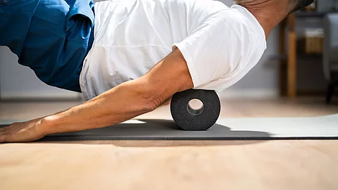 Ein Mann rollt seinen Rücken über eine Faszienrolle.