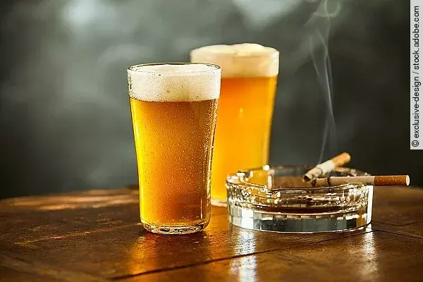 Auf einem Tisch stehen zwei Gläser Bier und ein Aschenbecher mit Zigaretten. 