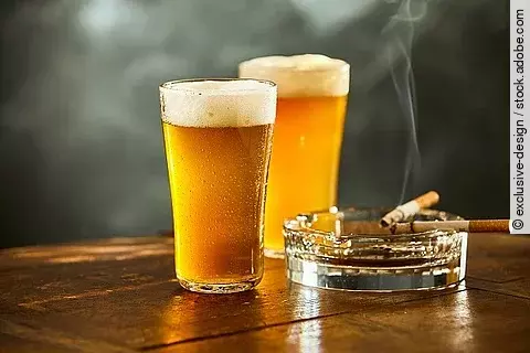 Auf einem Tisch stehen zwei Gläser Bier und ein Aschenbecher mit Zigaretten. 