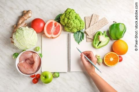 Frau schreibt in ihr Notizbuch, das umgeben ist von Obst und Gemüse.