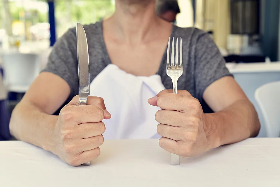 junge Frau wartet auf ihr Essen mit Besteck in der Hand vor einem leeren Teller