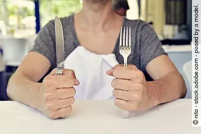 junge Frau wartet auf ihr Essen mit Besteck in der Hand vor einem leeren Teller