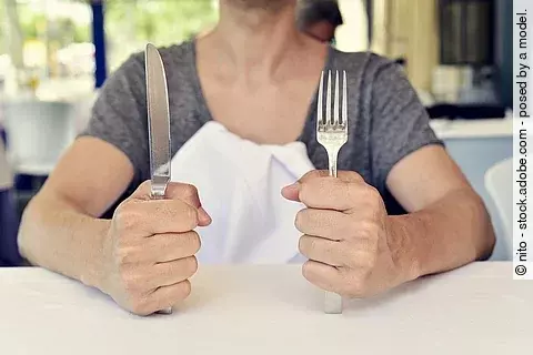 junge Frau wartet auf ihr Essen mit Besteck in der Hand vor einem leeren Teller