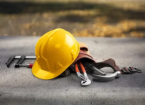 Gelber Sicherheitshelm und Werkzeuggürtel liegen auf einer Straße.