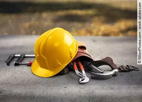 Gelber Sicherheitshelm und Werkzeuggürtel liegen auf einer Straße.