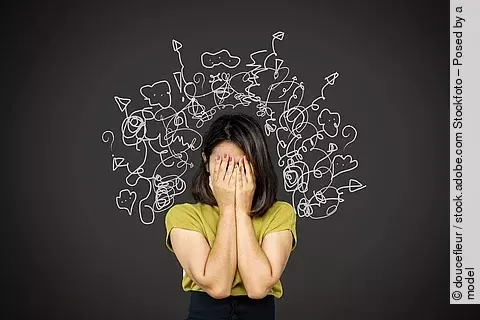 Frau hält sich die Hände vor das Gesicht vor schwarzem Hintergrund.