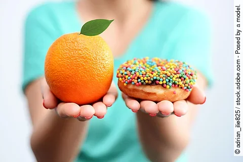 Junge Frau hält eine Orange und einen Donut in die Kamera