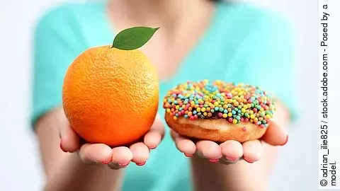 Junge Frau hält eine Orange und einen Donut in die Kamera