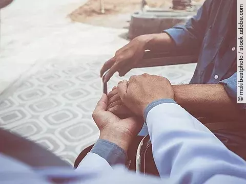 Arzt hält Patient im Rollstuhl die Hand.
