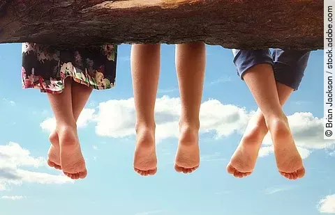 3 Kinder sitzen auf einem Baumstamm und lassen die Beine baumeln.